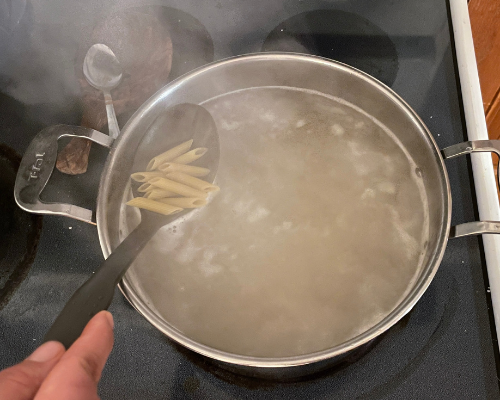 A pot on the stove boiling water with pasta in it